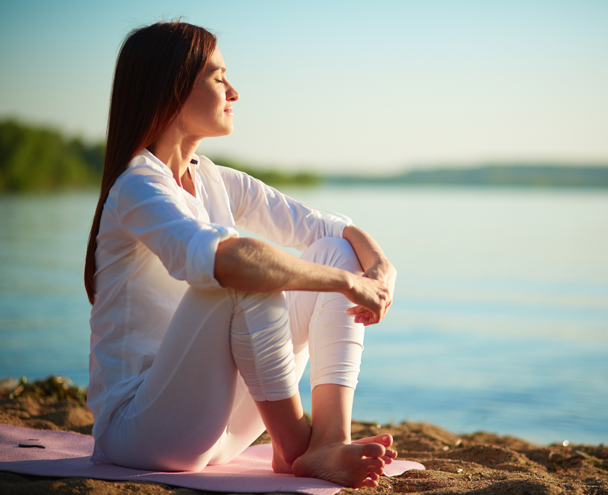 Femme méditant en position assise au bord de l'eau.